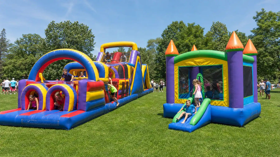 An inflatable obstacle course and a bounce house combo set up side by side at an outdoor community event
