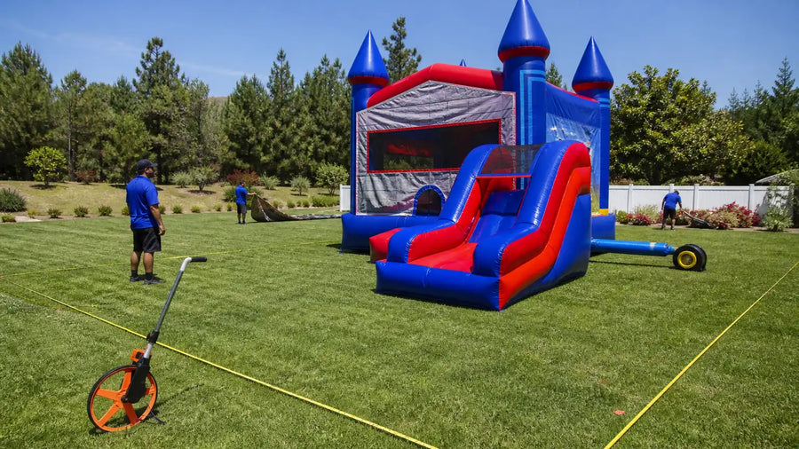 Crew measuring perimeter clearance around a commercial bounce house combo on a grass lot before setup