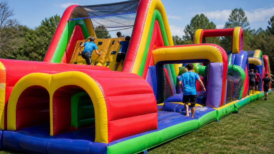 Participants racing through a large commercial inflatable obstacle course with a climbing wall at an outdoor team event