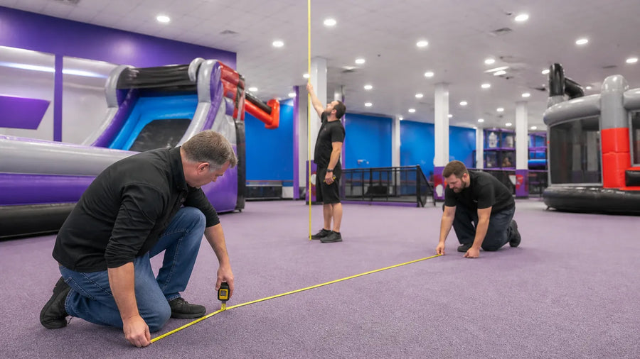 Crew measuring floor space and ceiling clearance for a commercial interactive inflatable game inside an indoor family entertainment center